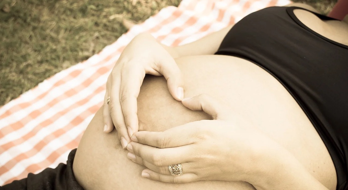 Mains posées sur le ventre arrondi d'une femme enceinte couchée dans l'herbe